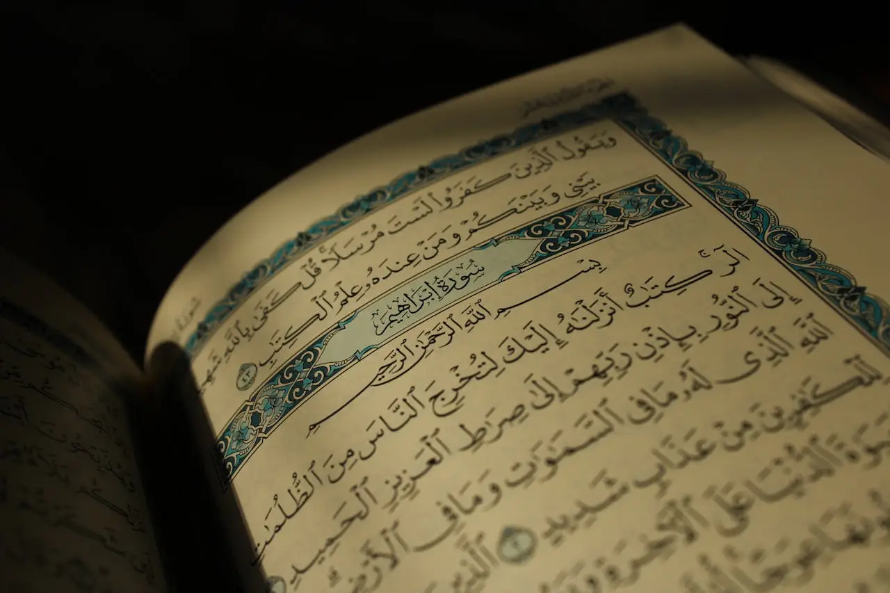 hero-img-01 Close-up of an open Quran displaying Arabic calligraphy under warm lighting, conveying spirituality.