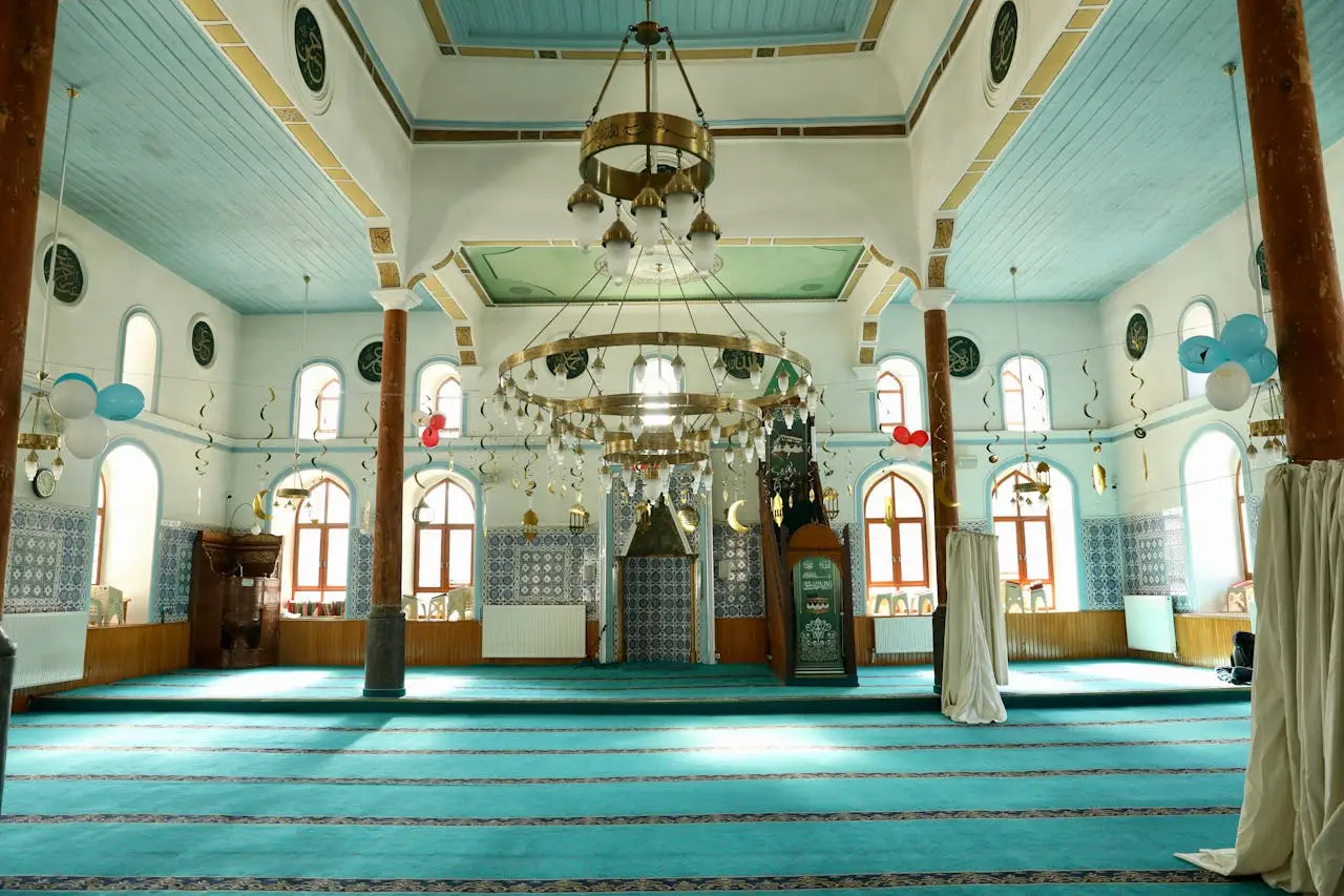 gallery-1 Tranquil interior view of a beautifully decorated mosque with ornate chandeliers and vibrant turquoise carpet.